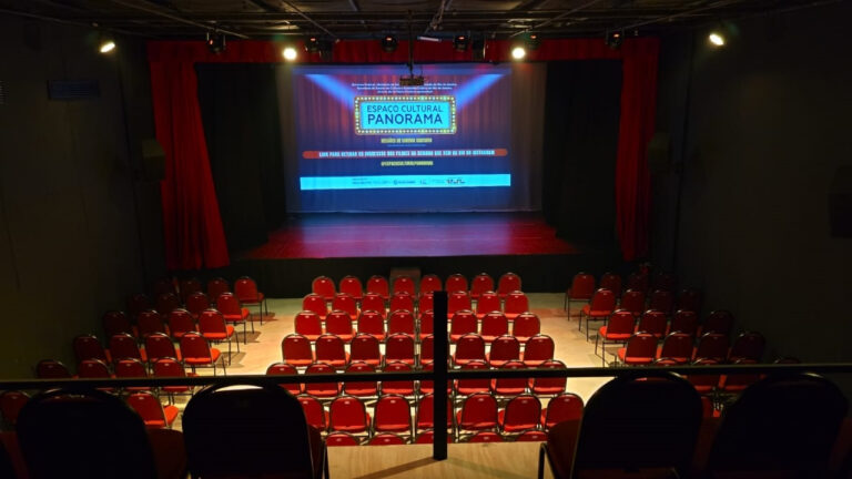 Pessoas em frente ao Espaço Cultural Panorama, em São Gonçalo, com livros e equipamentos de cinema, representando o novo corredor cultural.
