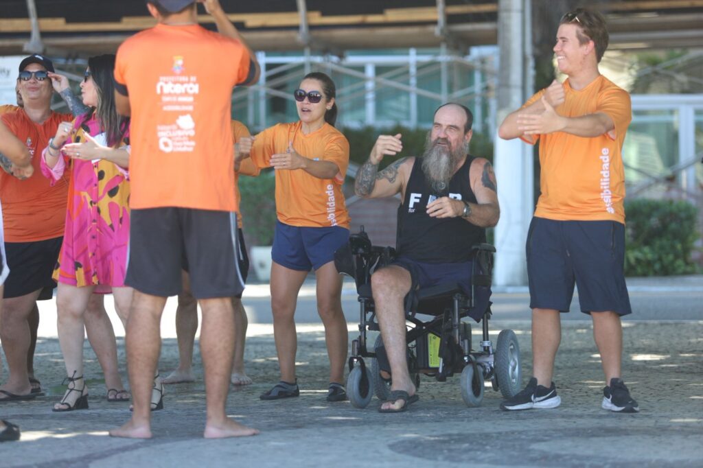 Pessoa em cadeira anfíbia sendo auxiliada por equipe no mar, em praia de Niterói. Projeto Praia Sem Barreiras.