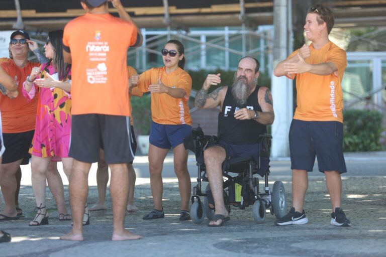 Pessoa em cadeira anfíbia sendo auxiliada por equipe no mar, em praia de Niterói. Projeto Praia Sem Barreiras.