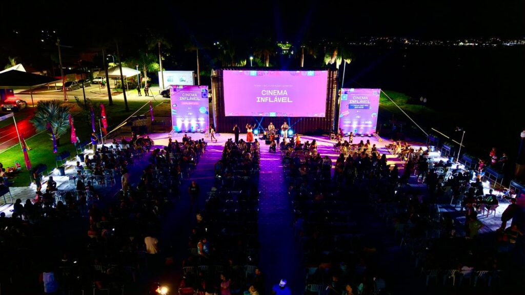 Pessoas assistem a filme em tela gigante inflável à noite, na orla do Parque Nanci, Maricá.