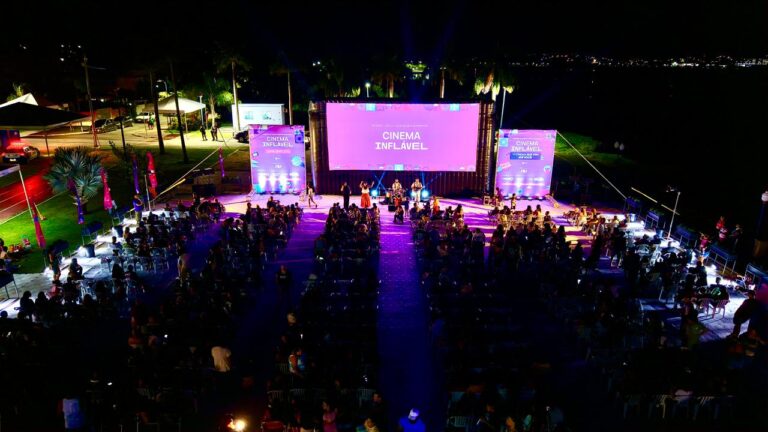 Pessoas assistem a filme em tela gigante inflável à noite, na orla do Parque Nanci, Maricá.