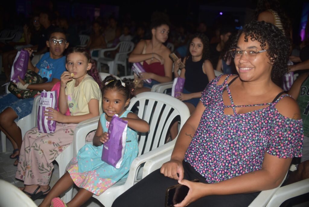 Pessoas assistindo a um filme em uma tela inflável ao ar livre em Maricá, durante o evento Cinema Inflável.