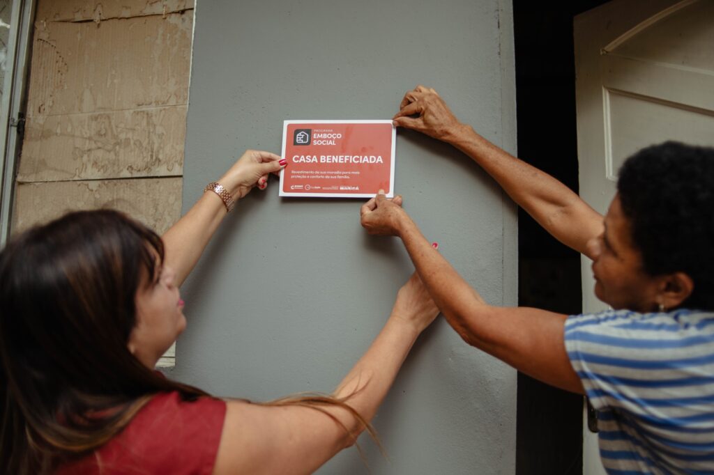 Pessoas em frente a casa reformada com emboço e pintura em Jacaroá, Maricá, pelo programa Emboço Social.