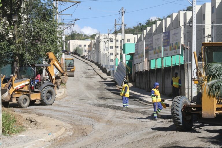 Obras de pavimentação e construção de calçadas em rua de São Gonçalo, com moradores observando o progresso.
