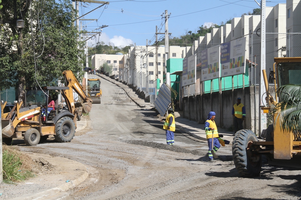Obras de pavimentação e construção de calçadas em rua de São Gonçalo, com moradores observando o progresso.