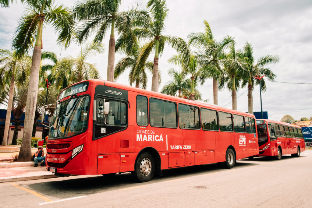 Ônibus Vermelhinho da EPT circulando em Maricá, com pessoas ao redor, simbolizando o transporte público gratuito.