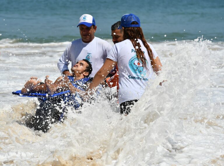 Pessoas em cadeiras anfíbias na Praia de Itaipu, Niterói, com equipe de apoio do Praia Sem Barreiras.
