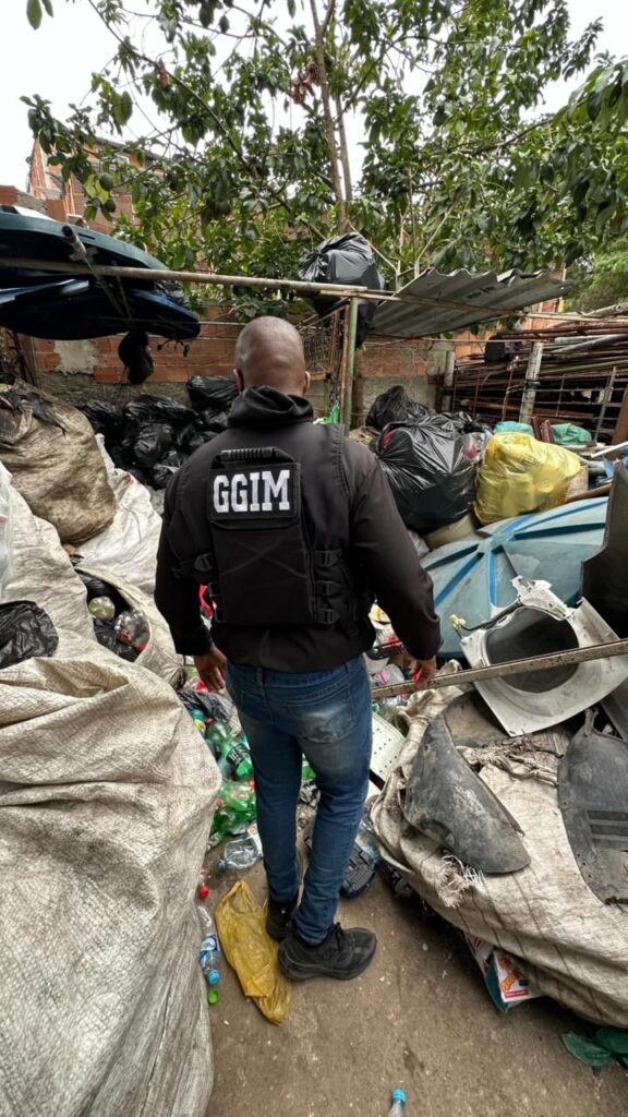 Agentes da Operação Asfixia fiscalizam ferro-velho clandestino no bairro Fonseca, em Niterói, com viaturas ao fundo.