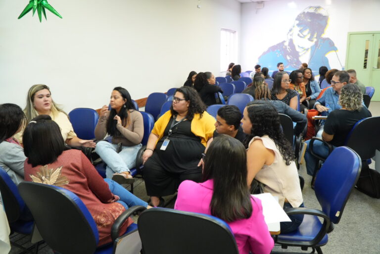 Dezenas de profissionais da Assistência Social de São Gonçalo participam de reunião em auditório, sentados em cadeiras e interagindo em grupos.