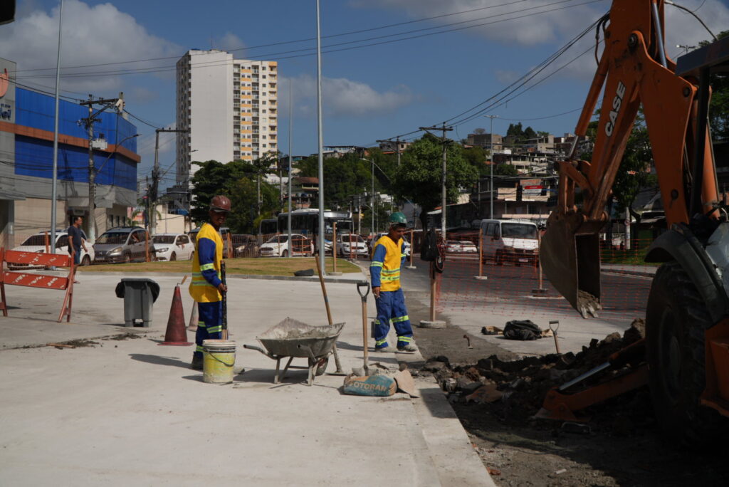 Obras do projeto MUVI em São Gonçalo, com trabalhadores e máquinas em rua, renovando asfalto e calçadas.