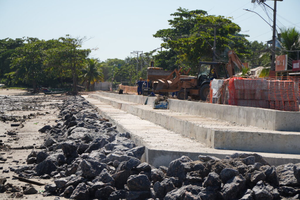 Vista aérea das obras de revitalização na Praia das Pedrinhas, São Gonçalo, com estrutura de pergolados e calçadão em construção.