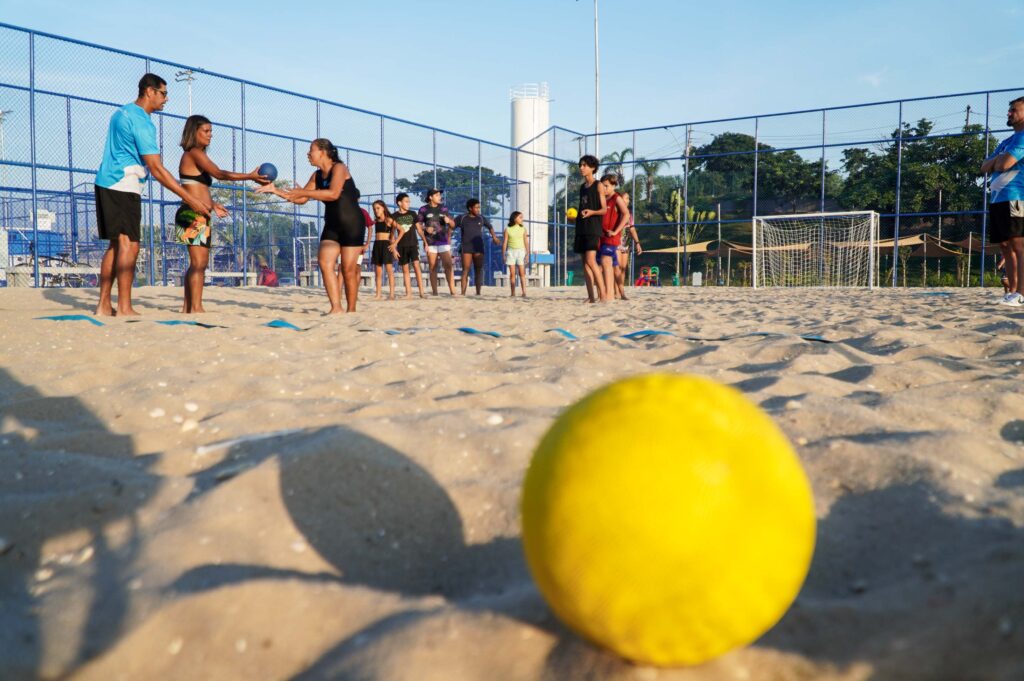 Crianças e adultos praticando handebol de areia em quadra no Parque RJ Nosso Sonho, São Gonçalo.