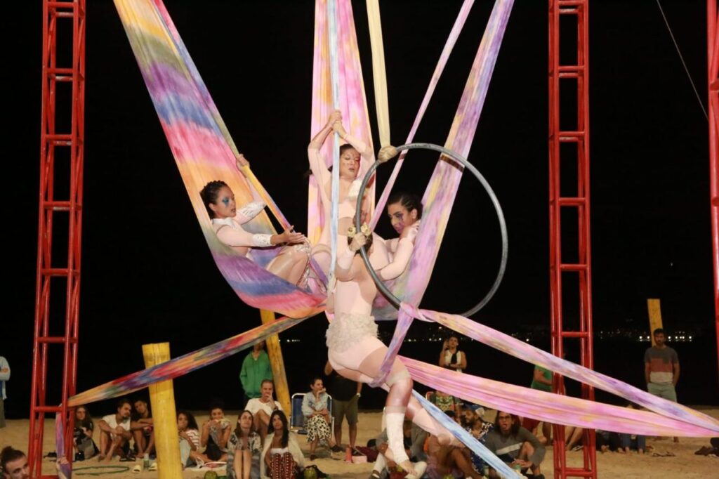 Espetáculo "Marcas do Passado" com performances aéreas na Praia de Icaraí, Niterói, abordando violência contra mulher.