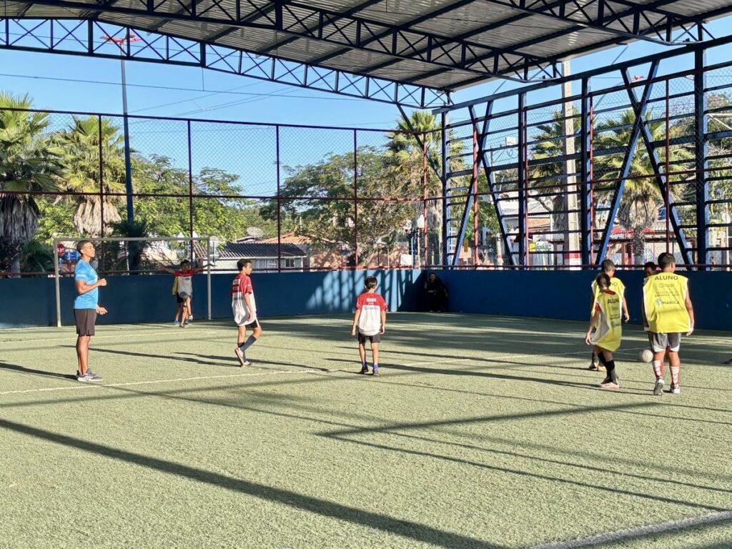 Crianças jogam futebol em campo em Maricá, representando as aulas gratuitas oferecidas pela Prefeitura.