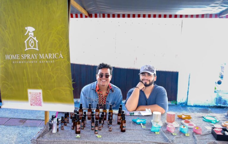 Pessoas em feira livre em Maricá, com barracas de produtos locais e plantas, promovendo agricultura familiar.