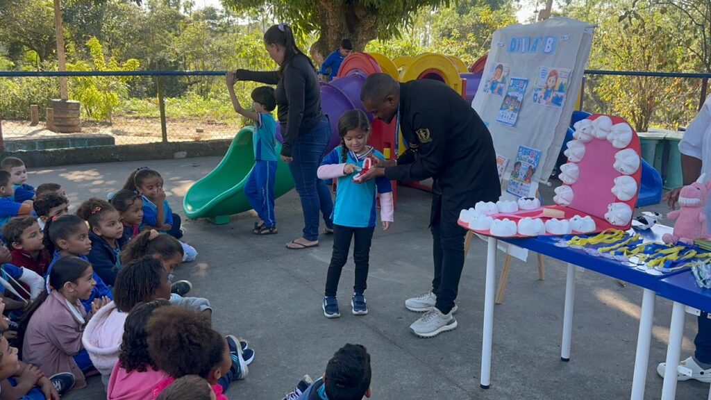 Crianças sorrindo enquanto recebem orientações de dentistas sobre saúde bucal em uma escola pública de São Gonçalo.