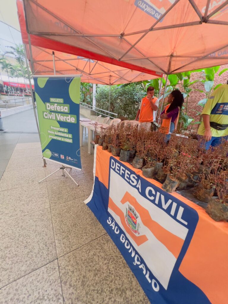 Agentes da Defesa Civil de São Gonçalo distribuem mudas e orientam moradores sobre preservação ambiental em shopping.