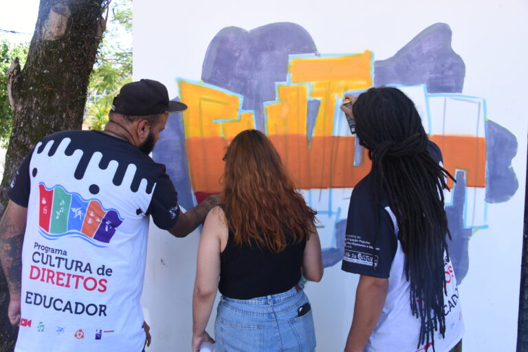 Alunos participando de oficina de grafite em Maricá, pintando um muro com spray e orientação
