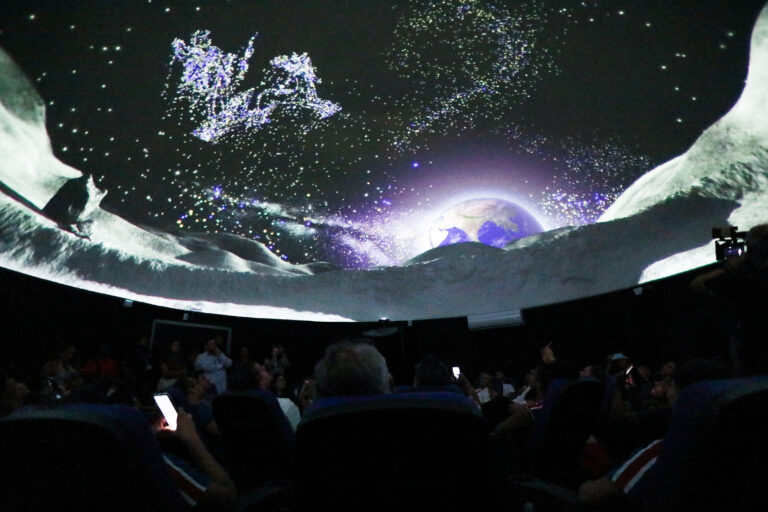 Pessoas observam projeção em cúpula do Planetário de Maricá durante programação de férias.