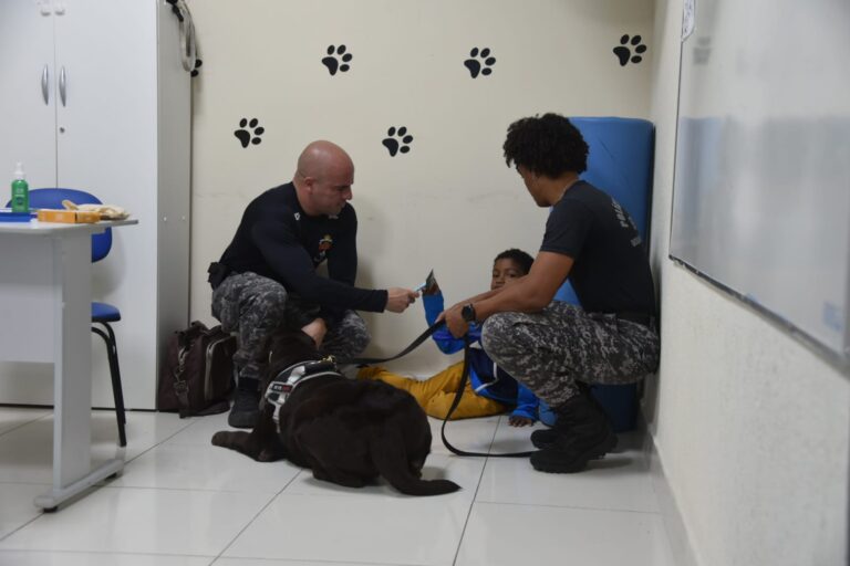 Criança interage com cão terapeuta durante sessão de cinoterapia em Maricá, com acompanhamento de profissional.