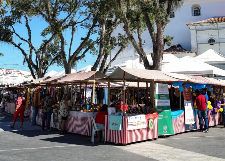 Pessoas em feira ao ar livre na Praça Orlando de Barros Pimentel, em Maricá, celebrando a Moeda Mumbuca.