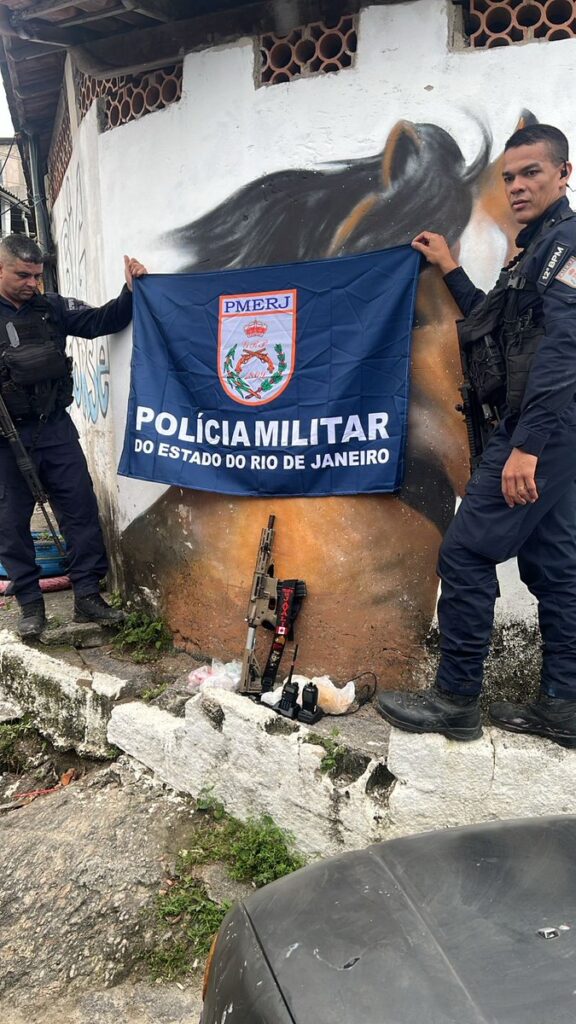Policiais militares exibem fuzil e drogas apreendidos em operação na Comunidade do Cavalão, em Niterói.