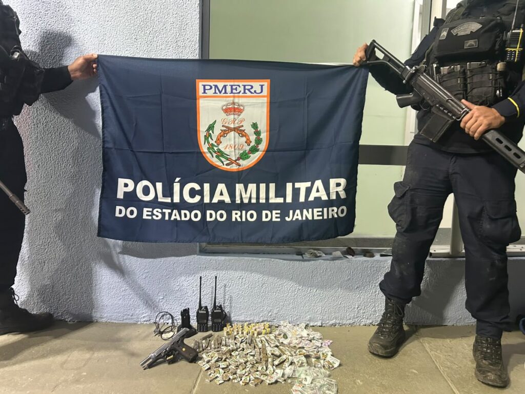 Policiais militares em operação de patrulhamento em área urbana, com viatura ao fundo, representando a ação da PMERJ.
