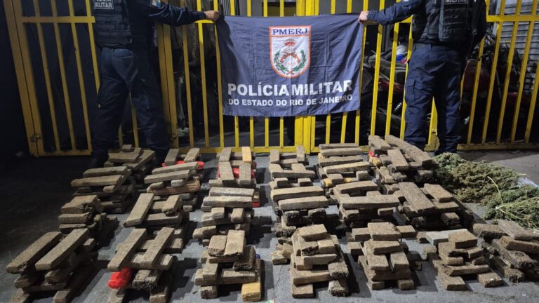 Policiais militares ao lado de grande quantidade de maconha em tabletes e equipamentos de estufa de drogas.