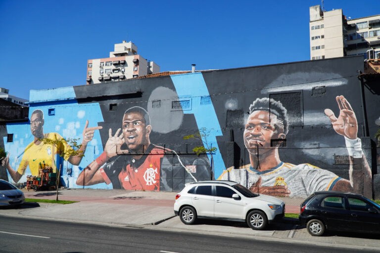 Painel grafitado gigante de Vini Jr. em São Gonçalo, mostrando fases da carreira do jogador.