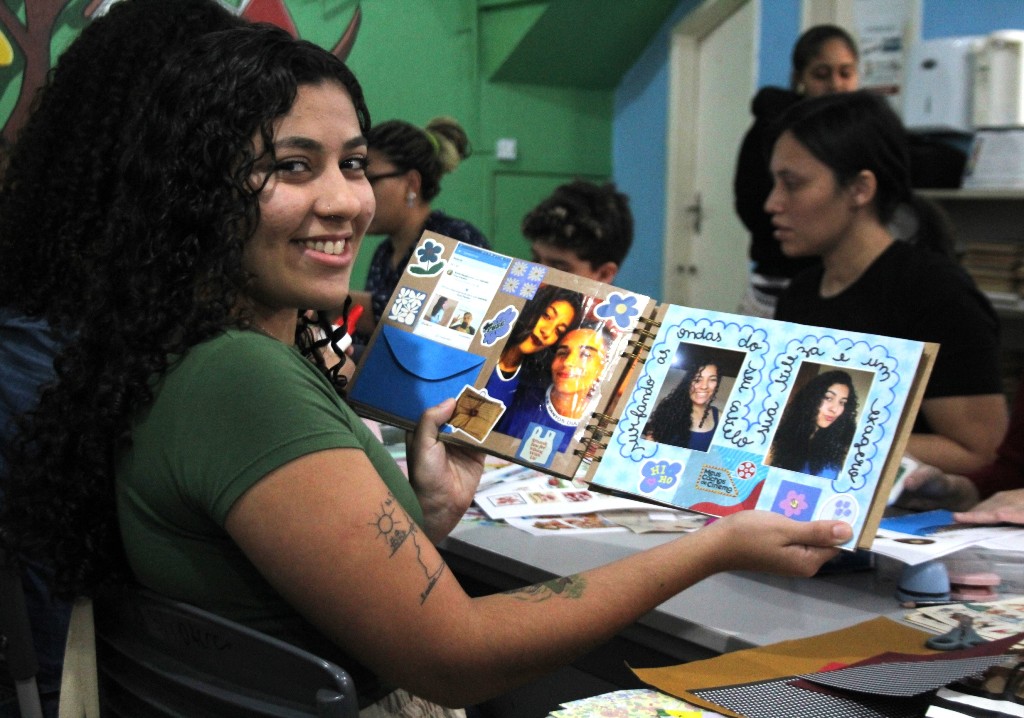 Oficina de scrapbook em São Gonçalo com participantes personalizando cadernos na Biblioteca Genebaldo Rosa.