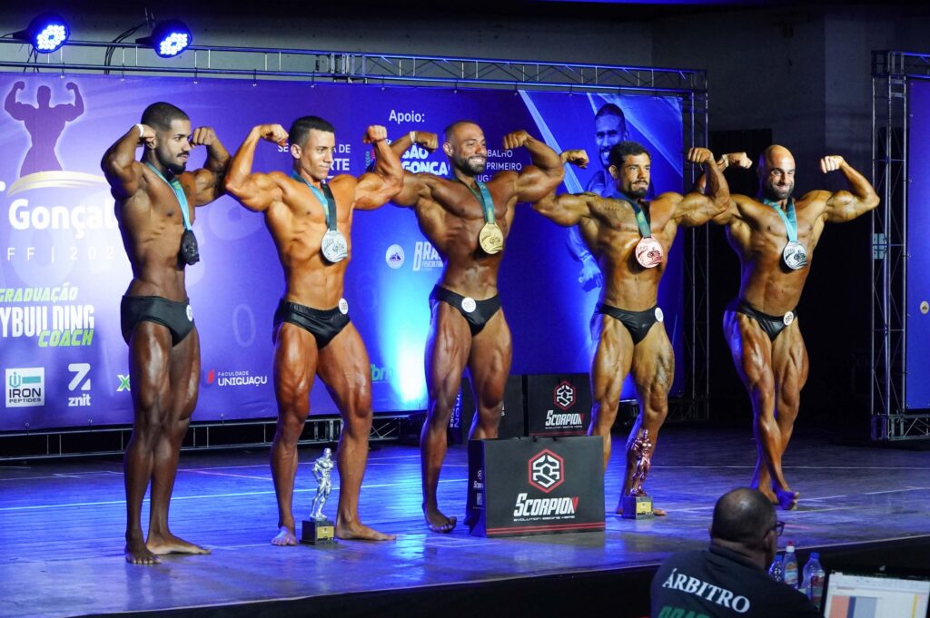 Atletas posam no palco exibindo musculatura durante o Campeonato de Fisiculturismo Mr. São Gonçalo no Clube Mauá.
