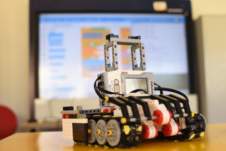 Alunos em aula de robótica em Maricá, trabalhando com kits de montagem e computadores para aprender tecnologia.