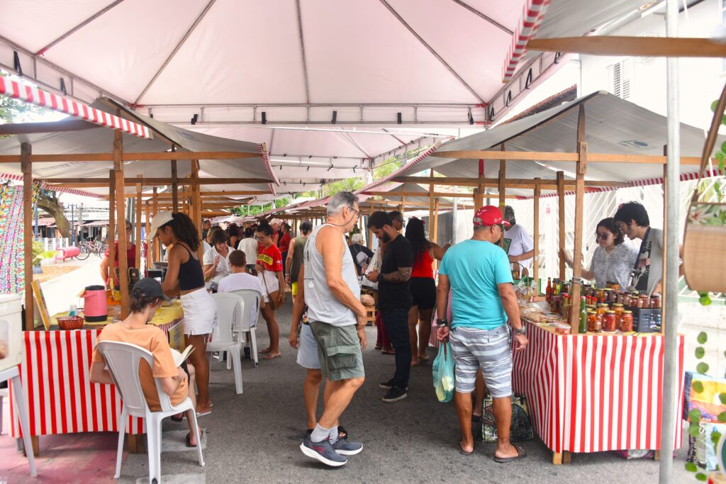 Pessoas comprando produtos frescos e artesanato em barracas da Feira da Agricultura Familiar em Maricá.