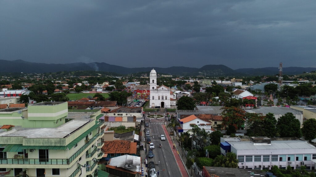 Homem caminha em praia de Maricá sob céu com poucas nuvens e ventos moderados