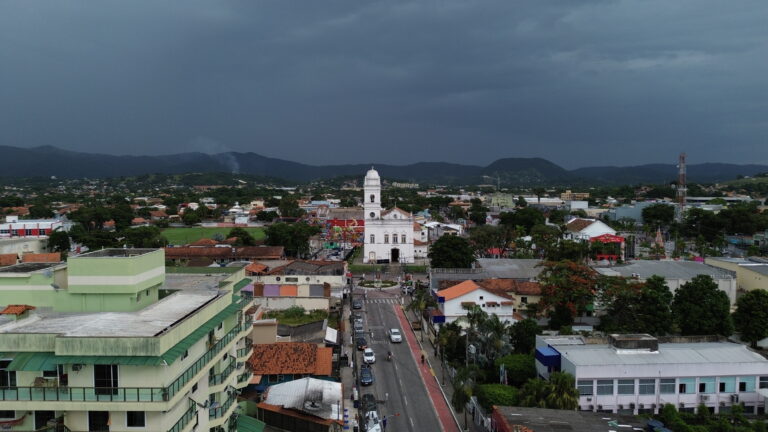 Homem caminha em praia de Maricá sob céu com poucas nuvens e ventos moderados