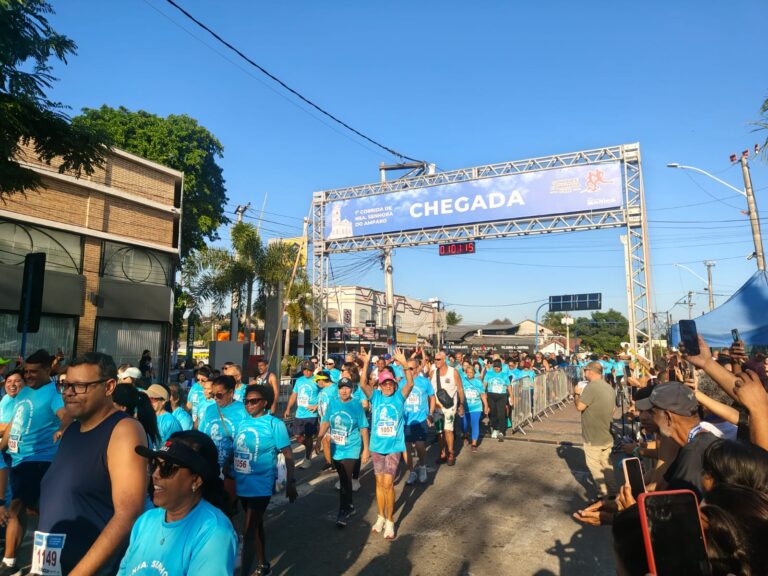 Participantes da Corrida da Padroeira em Maricá correndo em rua com público e prédios ao fundo.