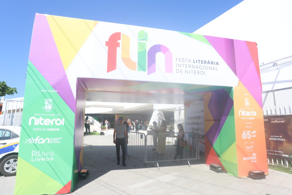 Pessoas em um evento literário, com livros e palestrantes, simbolizando a Festa Literária Internacional de Niterói (FLIN).