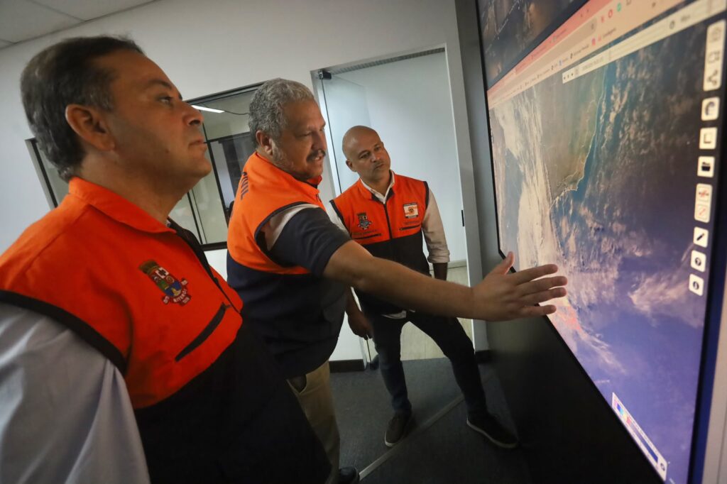 Equipe da Defesa Civil de Niterói monitora telas com dados meteorológicos em centro de operações.