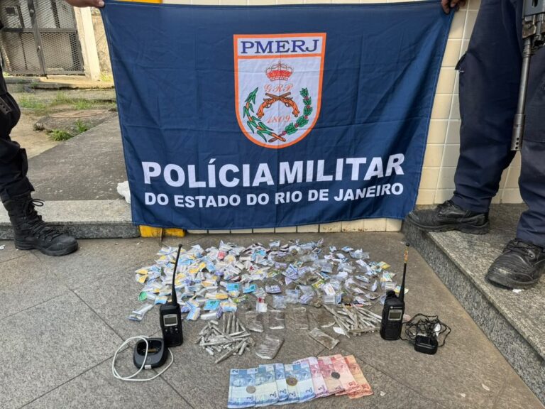 Policiais militares exibem drogas apreendidas, como maconha, cocaína e crack, junto com rádios e dinheiro em Niterói.