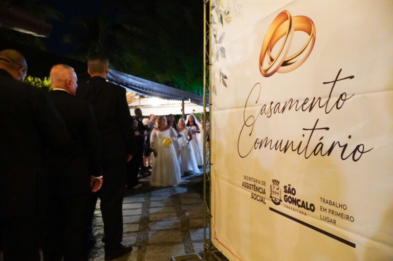 Casais sorrindo e abraçados durante a cerimônia do Casamento Comunitário em São Gonçalo, com decoração festiva.