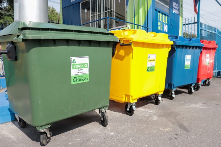 Lixo reciclável separado em containers em um ecoponto de São Gonçalo, com pessoas entregando materiais.