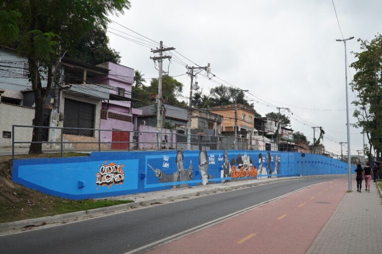 Painel artístico colorido em corredor viário de São Gonçalo, representando o Palacete do Mimi e artistas.