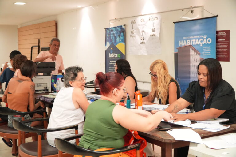 Pessoas entregando documentos em balcão de atendimento para programa habitacional em São Gonçalo.