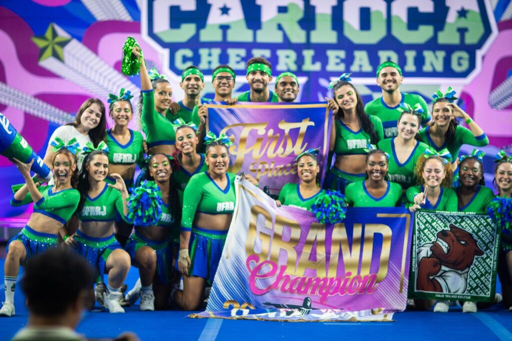 Equipe de cheerleading em apresentação de pirâmide humana com atletas uniformizados em ginásio.