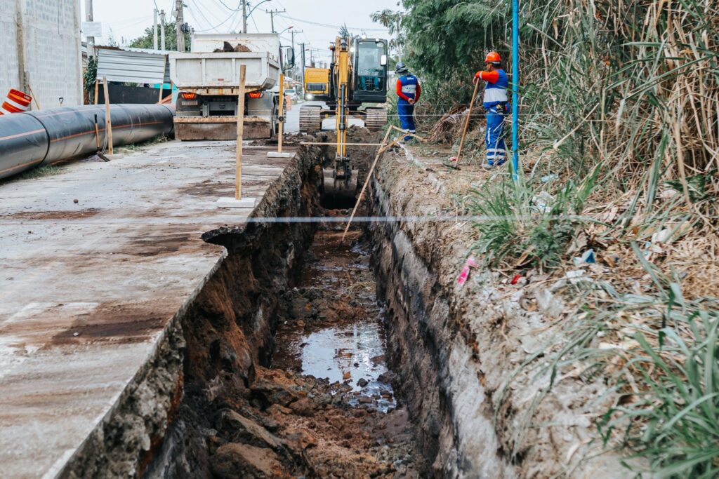 Obra de infraestrutura em Maricá, com tubulações e trabalhadores, mostrando o avanço da rede de esgoto.