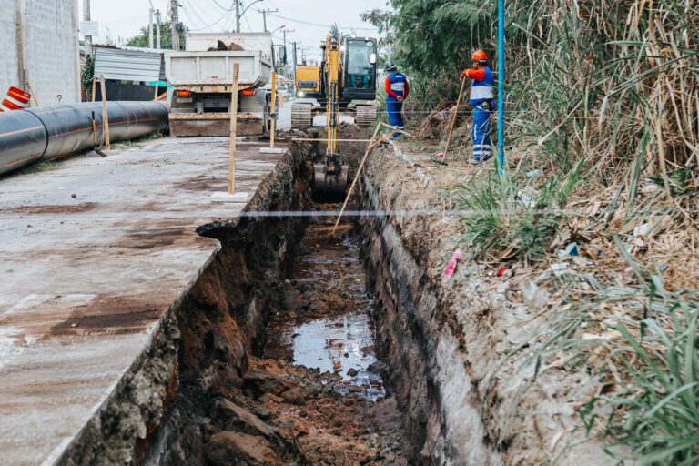 Obra de infraestrutura em Maricá, com tubulações e trabalhadores, mostrando o avanço da rede de esgoto.