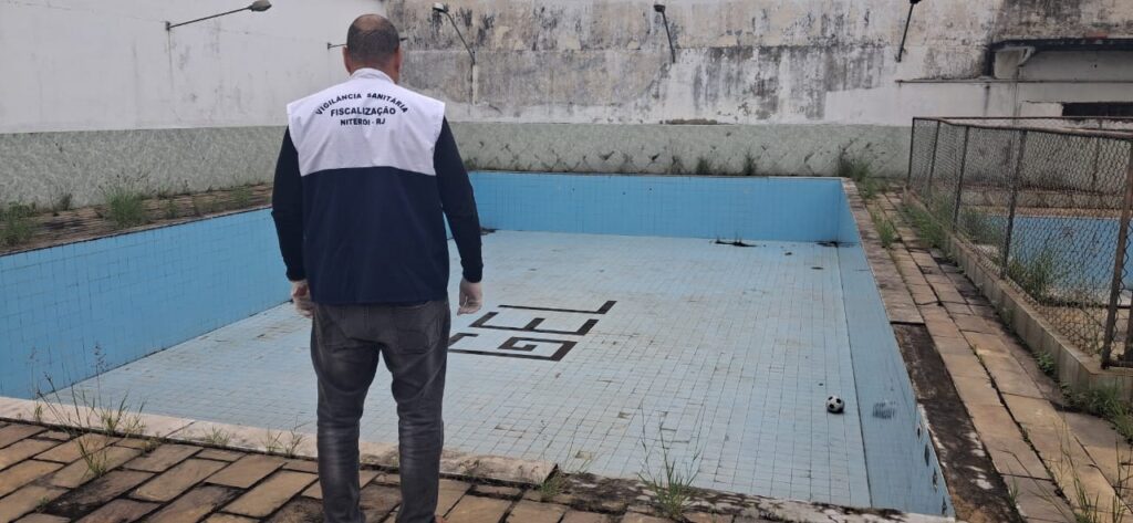 Agentes da fiscalização em frente a uma academia, com equipamentos de academia visíveis ao fundo.