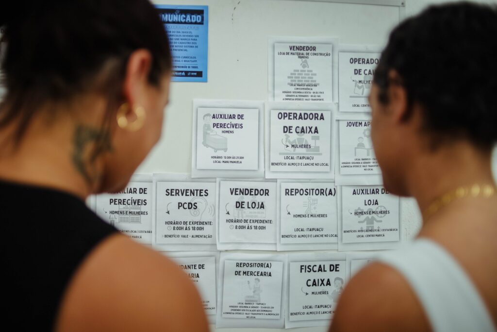 Pessoas consultam painel de vagas de emprego na Casa do Trabalhador de Maricá, buscando oportunidades.