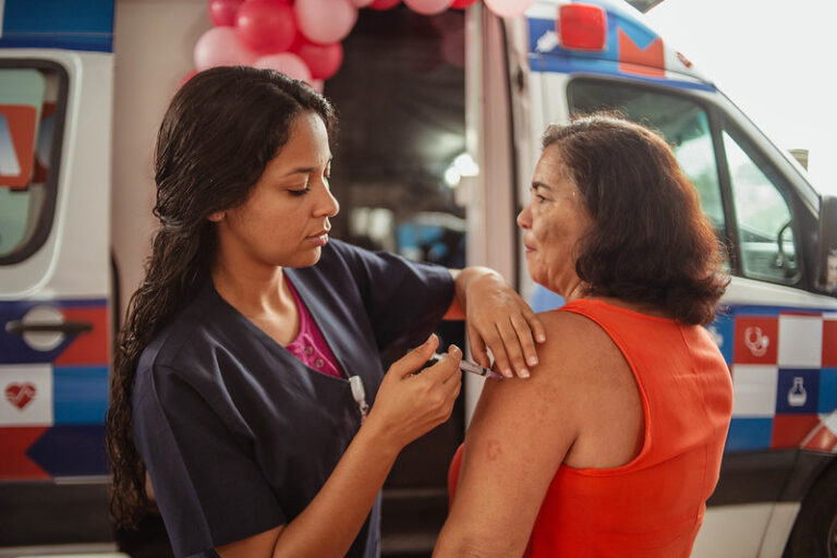 Mulheres sendo atendidas em ação do Outubro Rosa na quadra da União de Maricá, com profissionais de saúde.
