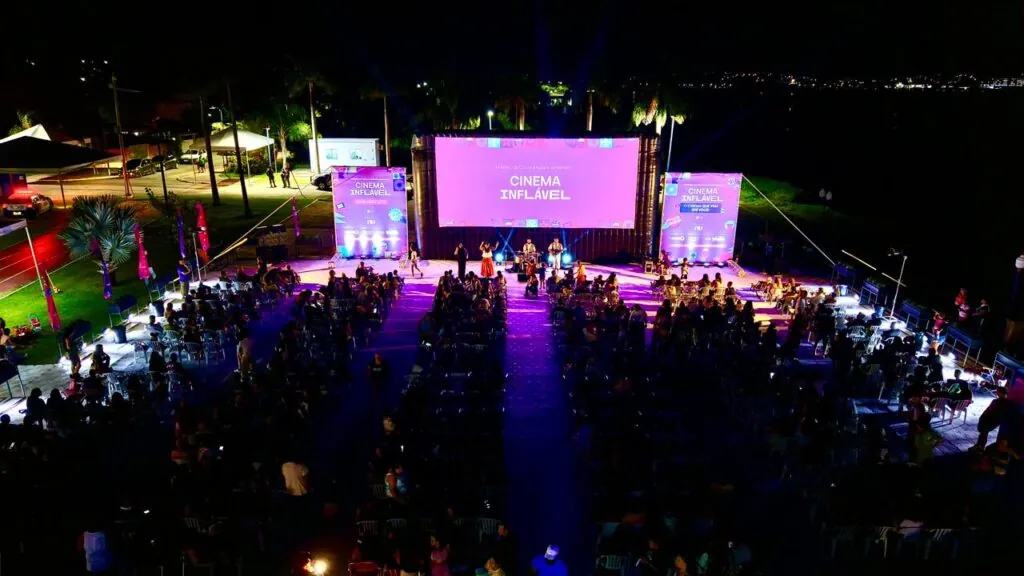 Pessoas assistem a filme em tela gigante inflável à noite, na orla do Parque Nanci, Maricá.